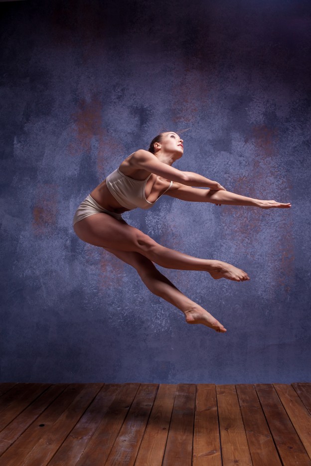 Young beautiful dancer in beige swimwear dancing on lilac background